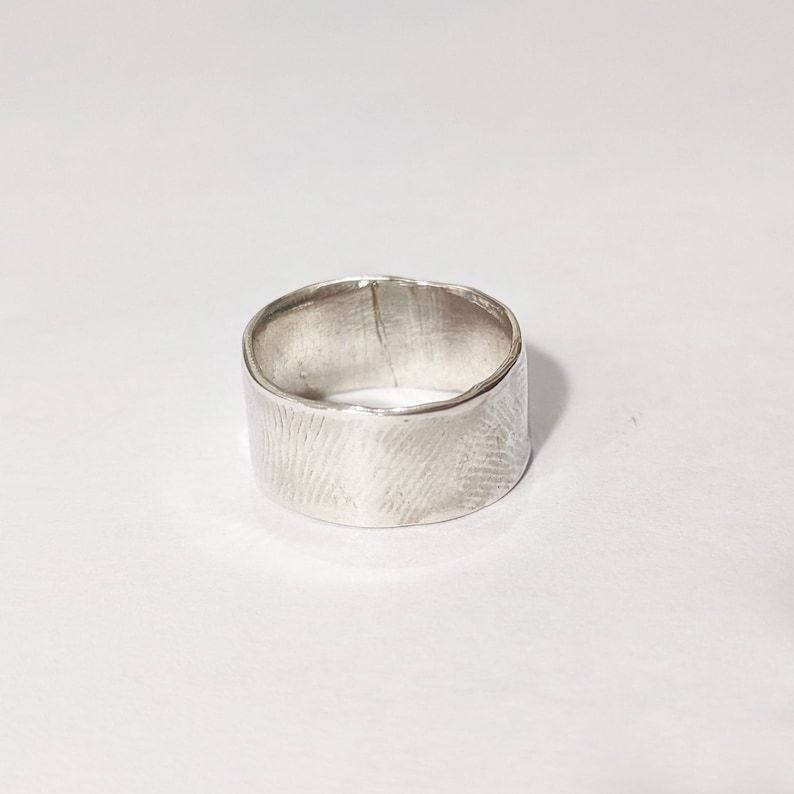 May include: A silver ring with a textured, hammered finish. The ring is wide and has a rounded band.