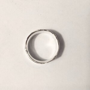 May include: A silver ring with a textured, hammered finish. The ring is round and has a smooth inner surface.