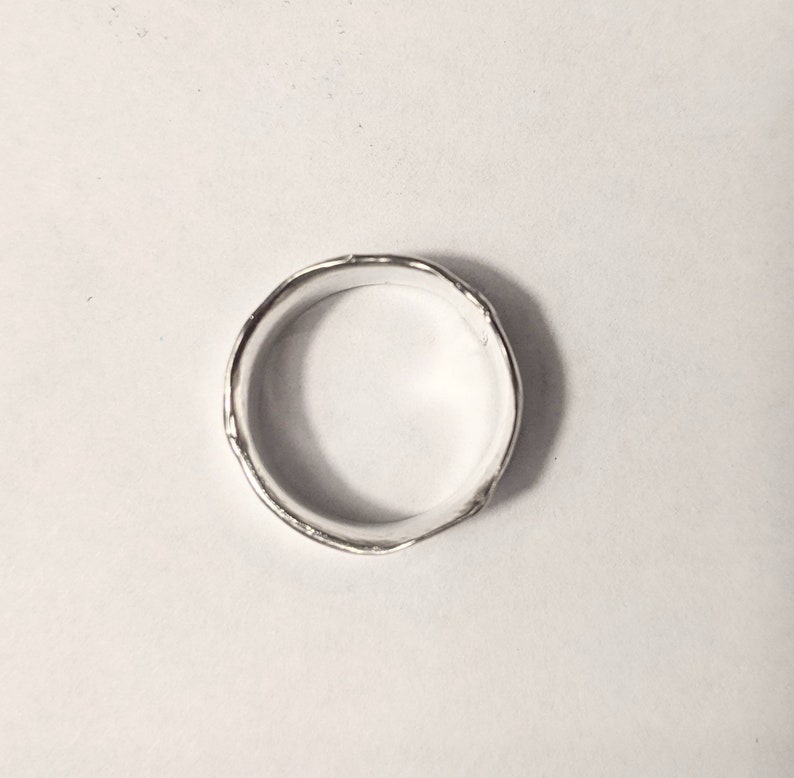 May include: A silver ring with a textured, hammered finish. The ring is round and has a smooth inner surface.