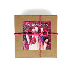 May include: A brown cardboard box tied with a pink ribbon. The box has a label that says "La mancina Jewelry".