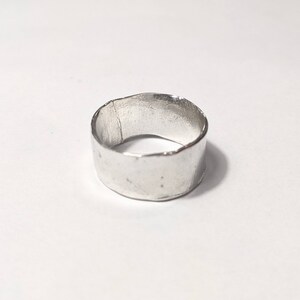 May include: A silver ring with a hammered finish. The ring is wide and has a rounded shape.