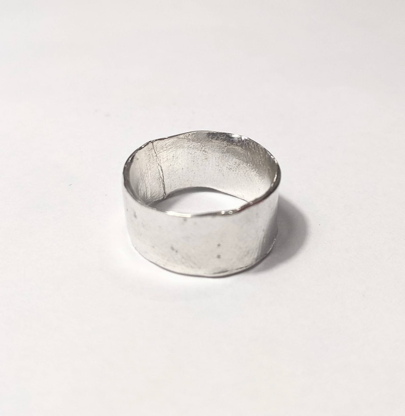 May include: A silver ring with a hammered finish. The ring is wide and has a rounded shape.