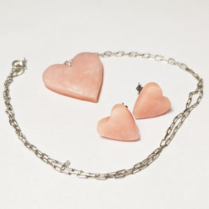 May include: A silver chain necklace with a pink heart pendant and matching pink heart earrings.