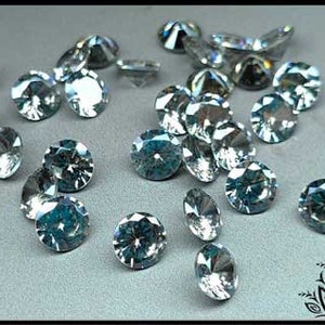 May include: A collection of round, faceted, clear, and light blue gemstones scattered across a surface. Each stone features a brilliant cut with multiple reflective surfaces that catch the light, creating a sparkling appearance with various sizes.