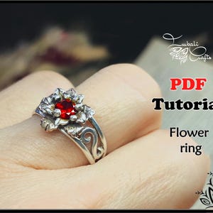 May include: A silver flower ring with a red gemstone center. The ring has a detailed floral design and is shown on a finger. The image also includes the text "PDF Tutorial Flower ring".