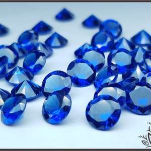May include: A collection of numerous loose, round-cut, faceted blue gemstones. Each stone features a brilliant, reflective surface with multiple triangular facets that catch the light, creating a deep, vibrant blue color across the entire group.