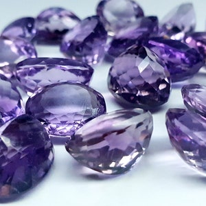 May include: A collection of loose, faceted amethyst gemstones in various shades of purple. Each stone features a polished, multi-faceted surface that reflects light, showcasing a clear, transparent quality and a brilliant, sparkling appearance.