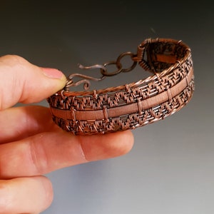 K&ouml;nnte beinhalten: Ein Armband aus Kupferdraht mit einem gewebten Muster. Das Armband hat einen Verschluss.