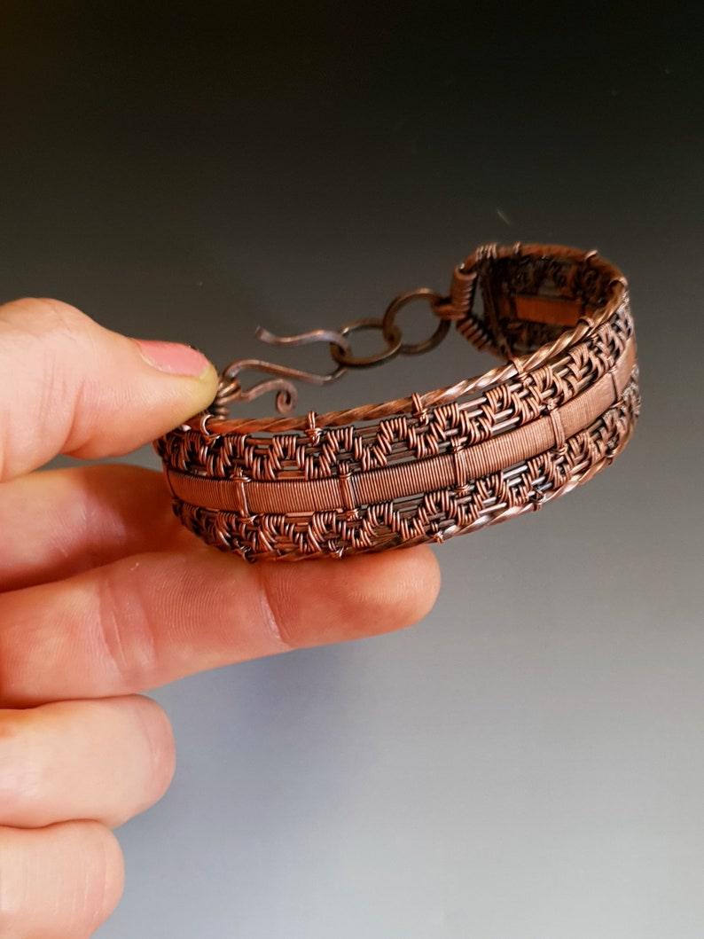 K&ouml;nnte beinhalten: Ein Armband aus Kupferdraht mit einem gewebten Muster. Das Armband hat einen Verschluss.