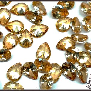 May include: A collection of loose, pear-shaped faceted gemstones in a warm, golden-amber hue. Each stone features a pointed top and rounded base with intricate geometric facets that reflect light, creating a sparkling, multi-dimensional appearance.
