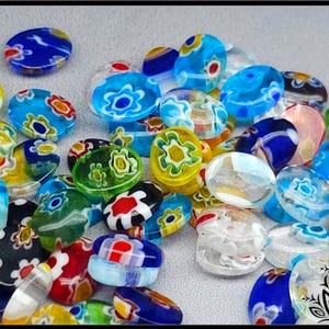 May include: A collection of small, oval-shaped glass beads featuring colourful millefiori floral patterns. The beads are translucent and opaque, displaying a variety of vibrant colours including blue, yellow, green, red, and white in various combinations.