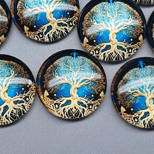 Pode incluir: Um conjunto de seis cabochões redondos de vidro com um design de árvore da vida dourado sobre um fundo azul. A árvore tem raízes e galhos intrincados.