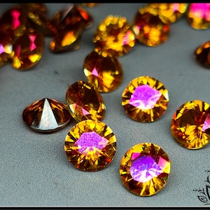 May include: A collection of round, faceted amber-colored gemstones with a vibrant iridescent finish. Each stone features a brilliant cut that reflects light, displaying warm golden-orange hues with bright pink and purple highlights throughout.