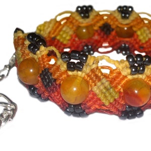 Puede incluir: Un brazalete tejido con cuentas de color naranja, amarillo y negro. El brazalete tiene una cadena plateada con una peque&ntilde;a cuenta en el extremo.