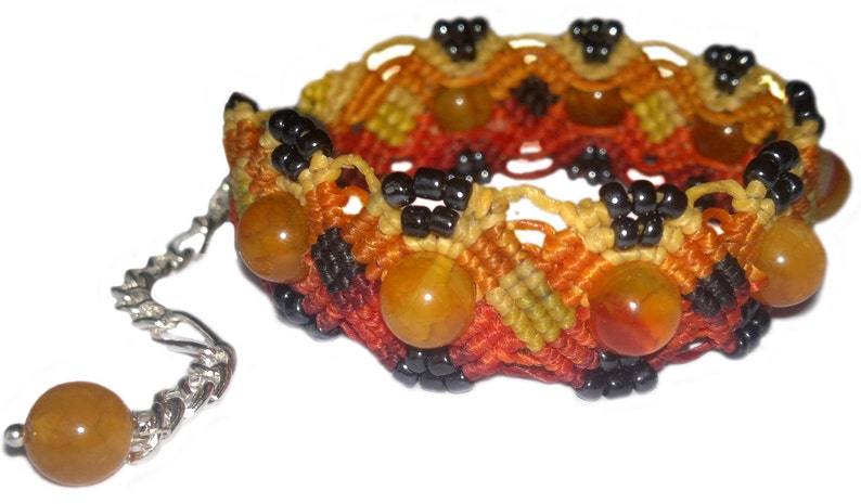 Puede incluir: Un brazalete tejido con cuentas de color naranja, amarillo y negro. El brazalete tiene una cadena plateada con una peque&ntilde;a cuenta en el extremo.