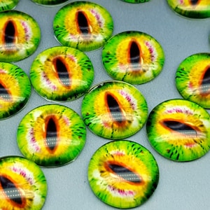 May include: A collection of circular glass cabochons featuring a detailed reptilian eye design. Each piece displays a vibrant yellow and green iris with a prominent black vertical pupil, creating a realistic animal eye effect for crafting projects.