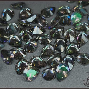 May include: A collection of loose, pear-shaped faceted gemstones with a dark, iridescent finish. Each stone features multiple geometric facets that reflect light, displaying subtle flashes of green, purple, and blue hues across their surfaces.