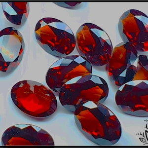 May include: A collection of loose, oval-cut gemstones in a deep, vibrant red color. Each stone features multiple faceted surfaces that reflect light, creating a brilliant, sparkling appearance across the various sizes and shapes of the stones.
