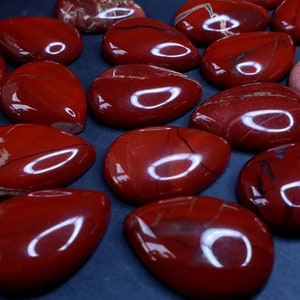 Puede incluir: Una colección de piedras de jaspe rojo pulidas, cada una con un patrón único de vetas y un acabado liso y brillante. Las piedras tienen forma de lágrima y tienen un color rojo intenso.