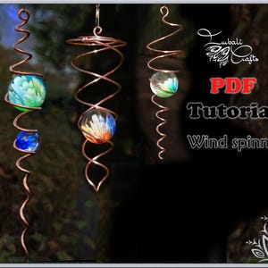 May include: Three copper wire wind spinners with colorful glass marbles. The spinners are suspended from the ceiling and are rotating in the wind. The image includes the text "PDF Tutorial Wind spinner".