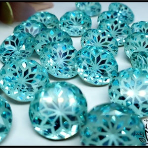 May include: A collection of faceted, round, light blue gemstones. Each gem has a detailed, geometric pattern within its surface, creating a sparkling effect. The gems are scattered across a white surface, with a soft focus on the background.
