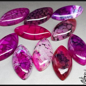 May include: Ten pink and purple agate cabochons with black and white patterns. The cabochons are shaped like a teardrop and have a smooth, polished surface.