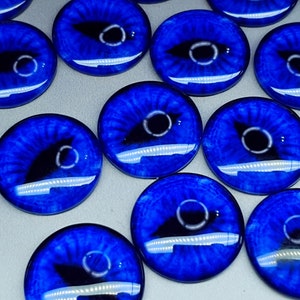May include: A collection of circular glass cabochons featuring a vibrant blue iris pattern with a black, elongated pupil. Each piece has a smooth, domed surface that creates a realistic eye effect with light reflections visible on the glossy finish.