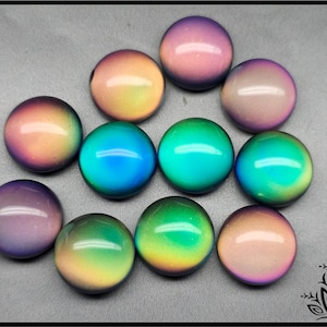 Könnte beinhalten: Eine Ansammlung von elf kreisförmigen, glatten, kuppelförmigen Cabochons mit einem farbwechselnden Verlaufseffekt. Die Oberflächen wechseln zwischen Violett-, Rosa-, Orange-, Gelb- und Türkistönen und erzeugen ein lebendiges, irisierendes Aussehen.