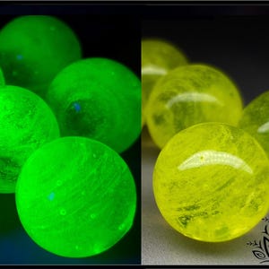 Op de afbeelding: Een gesplitste afbeelding toont gloeiende bollen. Links stralen groene bollen neonkleurig. Rechts zijn vergelijkbare bollen in geel te zien. De bollen hebben een textuur, mogelijk van glas of kristal. Donkere achtergrond.