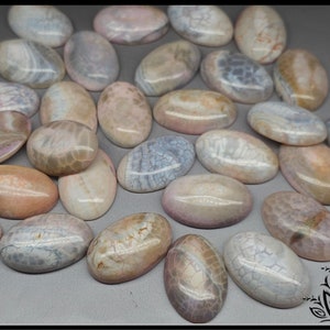 May include: A collection of smooth, oval-shaped cabochons featuring a variety of marbled and cracked patterns in soft shades of pink, beige, grey, and white. Each stone has a polished, glossy finish that reflects light across its rounded surface.