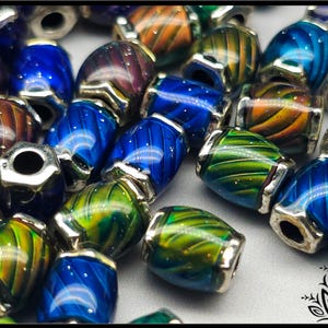 May include: A collection of barrel-shaped glass beads featuring swirling patterns in shades of blue, green, and orange. Each bead is accented with metallic silver-toned caps on both ends, creating a reflective and multi-colored appearance.