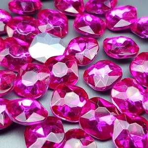 May include: A large quantity of pink, faceted, heart-shaped rhinestones. The rhinestones are scattered on a gray surface.