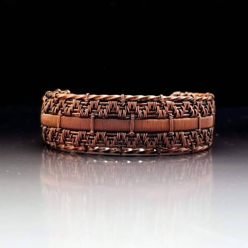 K&ouml;nnte beinhalten: Ein Armband aus Kupferdraht mit einem gewebten Design. Das Armband besteht aus mehreren Kupferdr&auml;hten, die miteinander verwoben sind, um ein geometrisches Muster zu erzeugen.