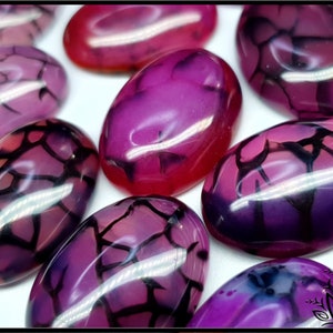 May include: A collection of oval-shaped, polished cabochons featuring a vibrant magenta and purple colour palette. Each stone displays a distinct black crackle pattern across its smooth, glossy surface, creating a network of dark, branching lines.