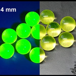 May include: A collection of spherical beads measuring 14 mm in diameter. The beads on the left side are a vibrant, glowing neon green against a dark blue background, while the beads on the right are a pale, translucent yellow-green.