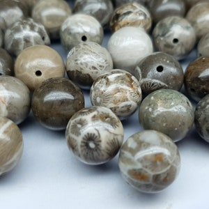 May include: A selection of spherical beads in shades of grey, brown, and cream. The beads have a natural, textured appearance with visible patterns. Each bead has a small hole, suggesting they are for stringing or crafting.