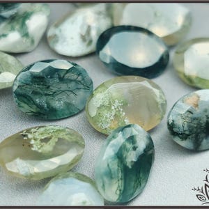 May include: A collection of oval-shaped moss agate gemstones featuring faceted surfaces. Each stone displays translucent white and pale green hues with dark green, branch-like inclusions throughout the mineral structure, creating a unique pattern in every piece.