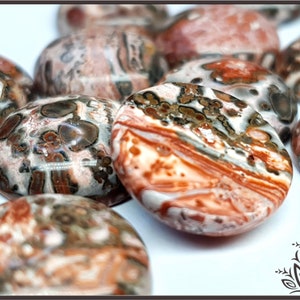 May include: A collection of oval-shaped, polished, natural stone cabochons. The stones are a mix of brown, white, and red with a swirling, marbled pattern.
