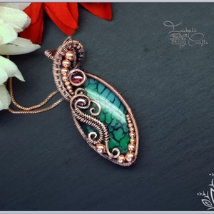 May include: A wire-wrapped pendant featuring a marquise-shaped green crackle agate stone, a small round dark red gemstone, and copper wire detailing. The pendant is suspended from a copper chain and includes the text Lubali Crafts.