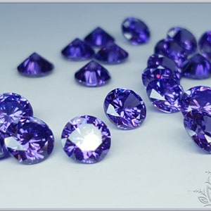 May include: A collection of round, brilliant-cut purple gemstones scattered across a light surface. Each stone features multiple facets that reflect light, creating a sparkling effect with deep violet hues and bright white highlights throughout.