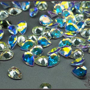 May include: A collection of loose, pear-shaped faceted crystals with an iridescent finish. Each crystal displays a spectrum of colors, including vibrant blues, yellows, and clear tones, reflecting light across their multiple angled surfaces.