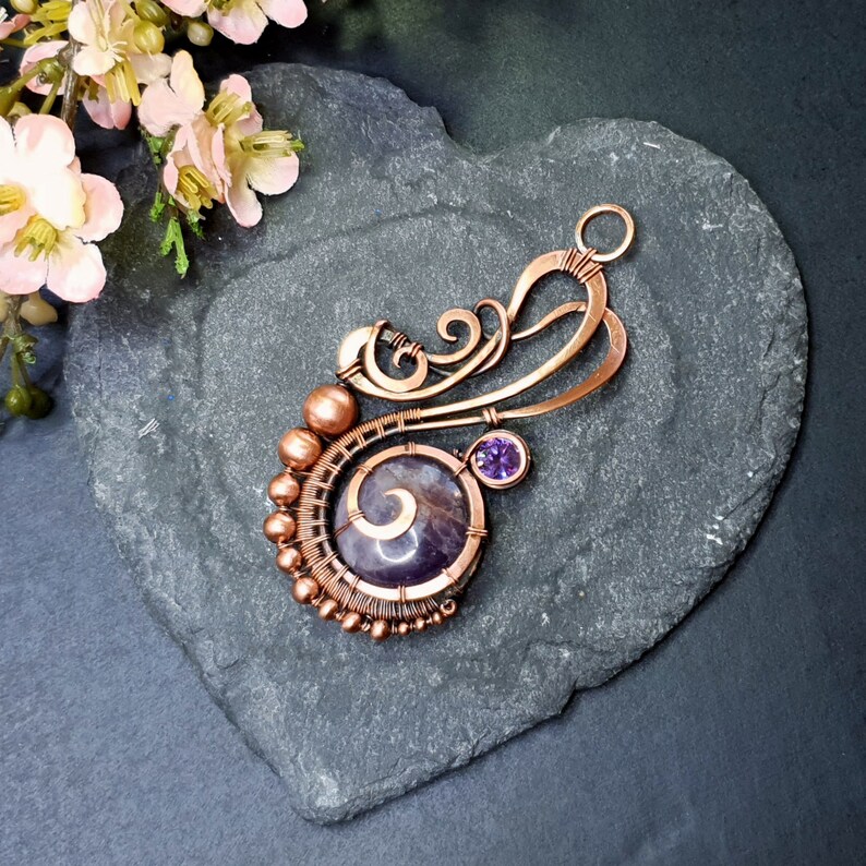 Peut inclure: Un pendentif en fil de cuivre enroul&eacute; avec une pierre d'am&eacute;thyste violette et une petite pierre pr&eacute;cieuse violette. Le pendentif a un design d&eacute;licat et complexe avec un motif en spirale.