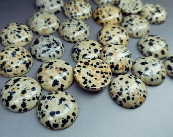 May include: A collection of round, smooth cabochons featuring a cream-colored base with irregular black spots, resembling a dalmatian pattern. Each piece has a polished, glossy finish and a domed top, arranged in a scattered group.