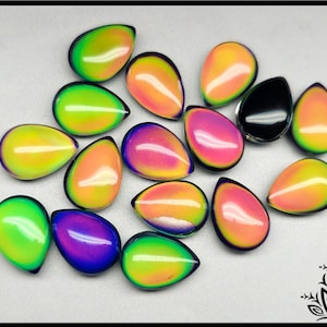 May include: A collection of teardrop-shaped cabochons in various colors, including green, yellow, orange, pink, purple, and black. The cabochons have a glossy finish and are arranged on a light-colored surface. These could be used for jewelry making.