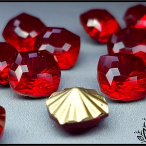 May include: A group of red glass gems with a gold metal decorative piece. The gems are faceted and have a shiny finish.