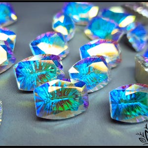 May include: A collection of faceted, oval-shaped glass cabochons featuring an iridescent finish that reflects vibrant shades of blue, green, and purple. Each piece displays a clear, multi-faceted surface with a radiant, light-catching quality.