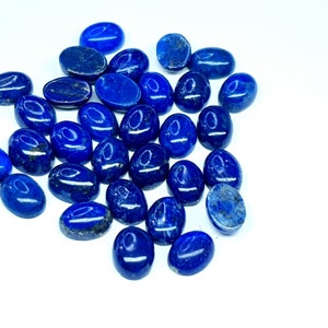 May include: A collection of oval-shaped, polished lapis lazuli gemstones. The stones are a deep blue colour with flecks of gold pyrite.