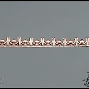 Peut inclure: Gros plan d'une garniture métallique de couleur cuivre avec un motif répétitif d'arches arrondies et de petits cercles.