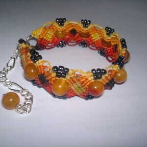 Puede incluir: Un brazalete trenzado con una cadena de plata y cuentas de color &aacute;mbar. El brazalete est&aacute; hecho con hilos negros, naranja y amarillos.