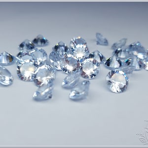 May include: A collection of loose, round-cut, clear faceted gemstones. Each stone features a brilliant, multi-faceted surface that reflects light, creating bright white highlights and subtle blue tones across the group of small, sparkling, transparent crystals.